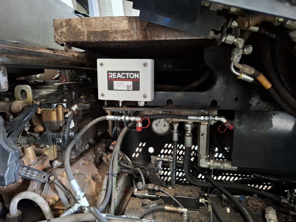 REACTON fire suppression system nozzles installed inside the hydraulic equipment compartment of a PONSSE Scorpion harvester in a workshop setting, showing detailed close-up of mounted fire protection components.