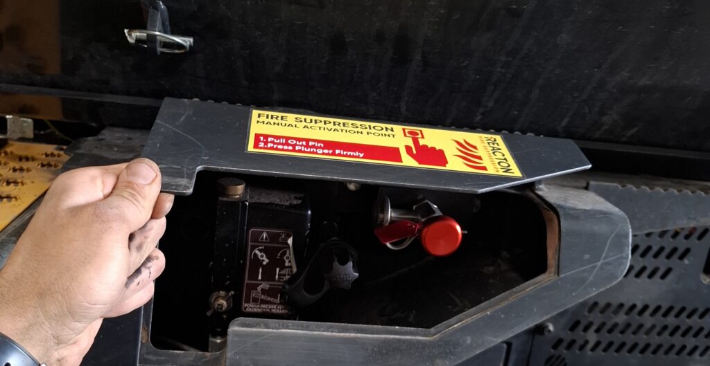 Manual activation valve of a REACTON fire suppression system installed on a PONSSE Scorpion harvester in a workshop, showing the emergency trigger component used for manual system discharge.